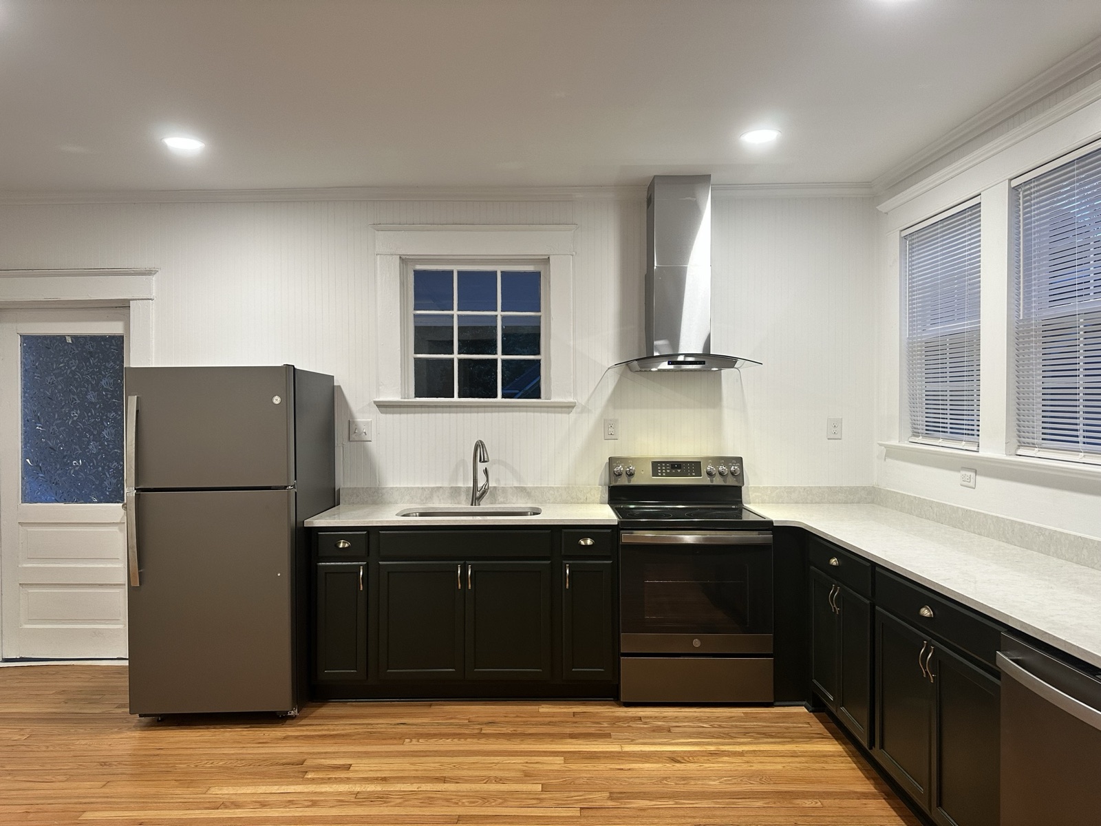 Renovated kitchen with charcoal cabinets, slate refrigerator, stainless chimney range hood, and a window over the sink