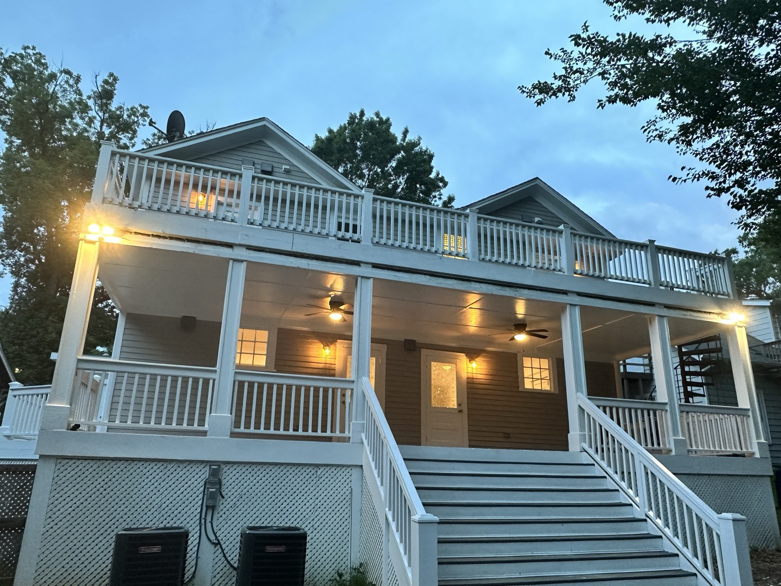 Rear elevation of 1110 Glenwood Ave at twilight, with a two-story covered porch, white railings, twin staircases, and lit lanterns