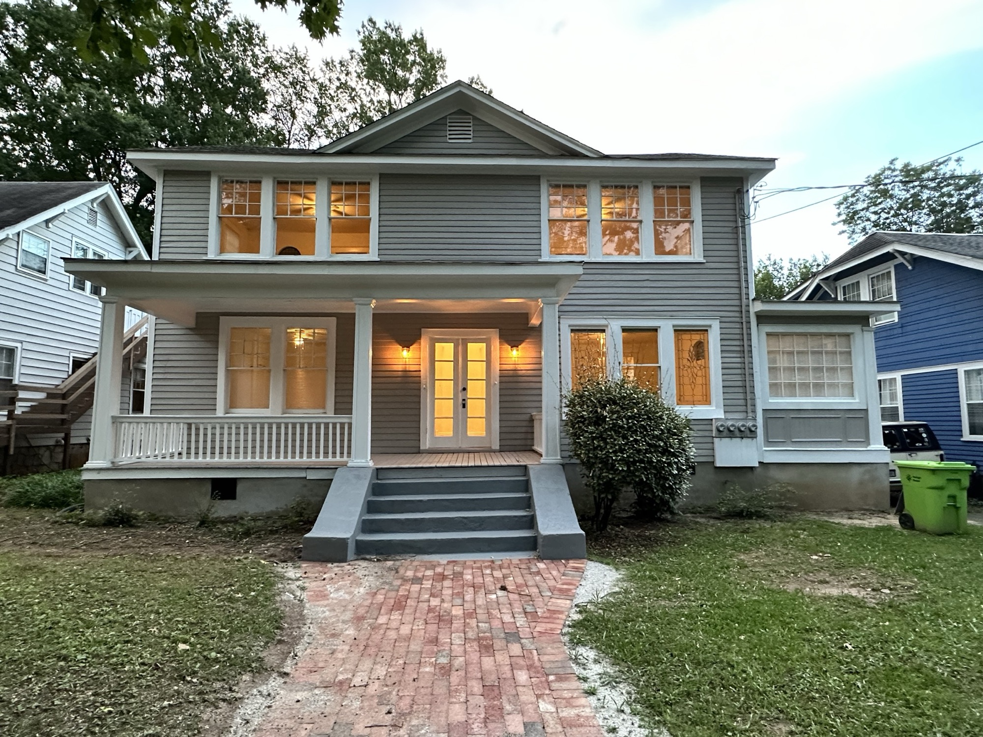 Twilight view of the Wallin-Trull House at 1110 Glenwood Ave, a two-story historic home with a full-width front porch, warm interior lights glowing, and a brick walkway leading to the steps